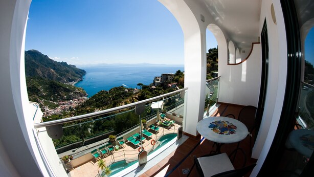 Un balcon avec vue sur la mer, une piscine et des chaises longues.
