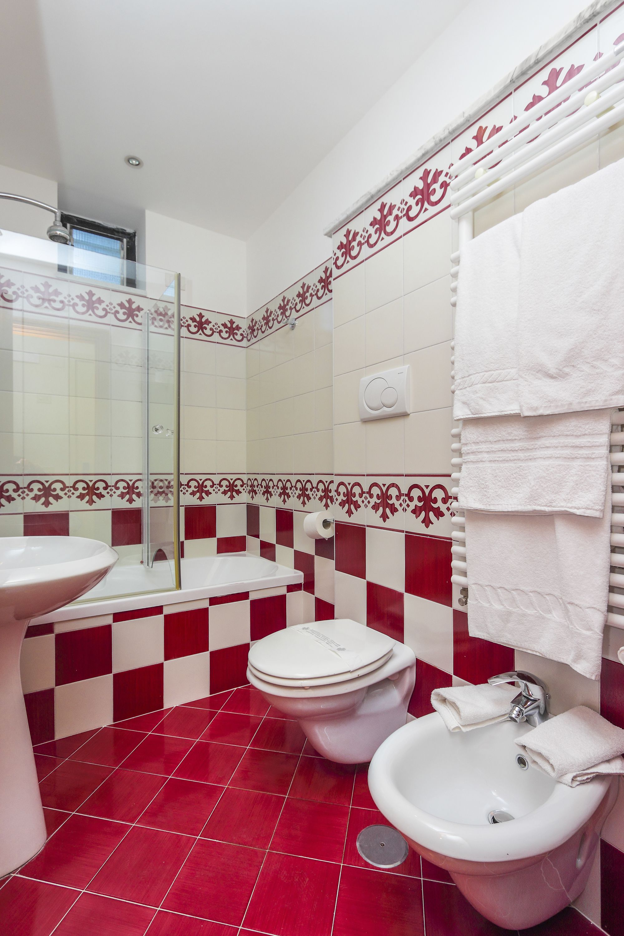 A bathroom with a red and white checkered floor, a white sink, a toilet, and a bidet.