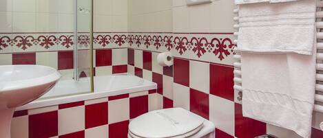 Une salle de bain avec un sol à carreaux rouges et blancs, un lavabo blanc, des toilettes et un bidet.