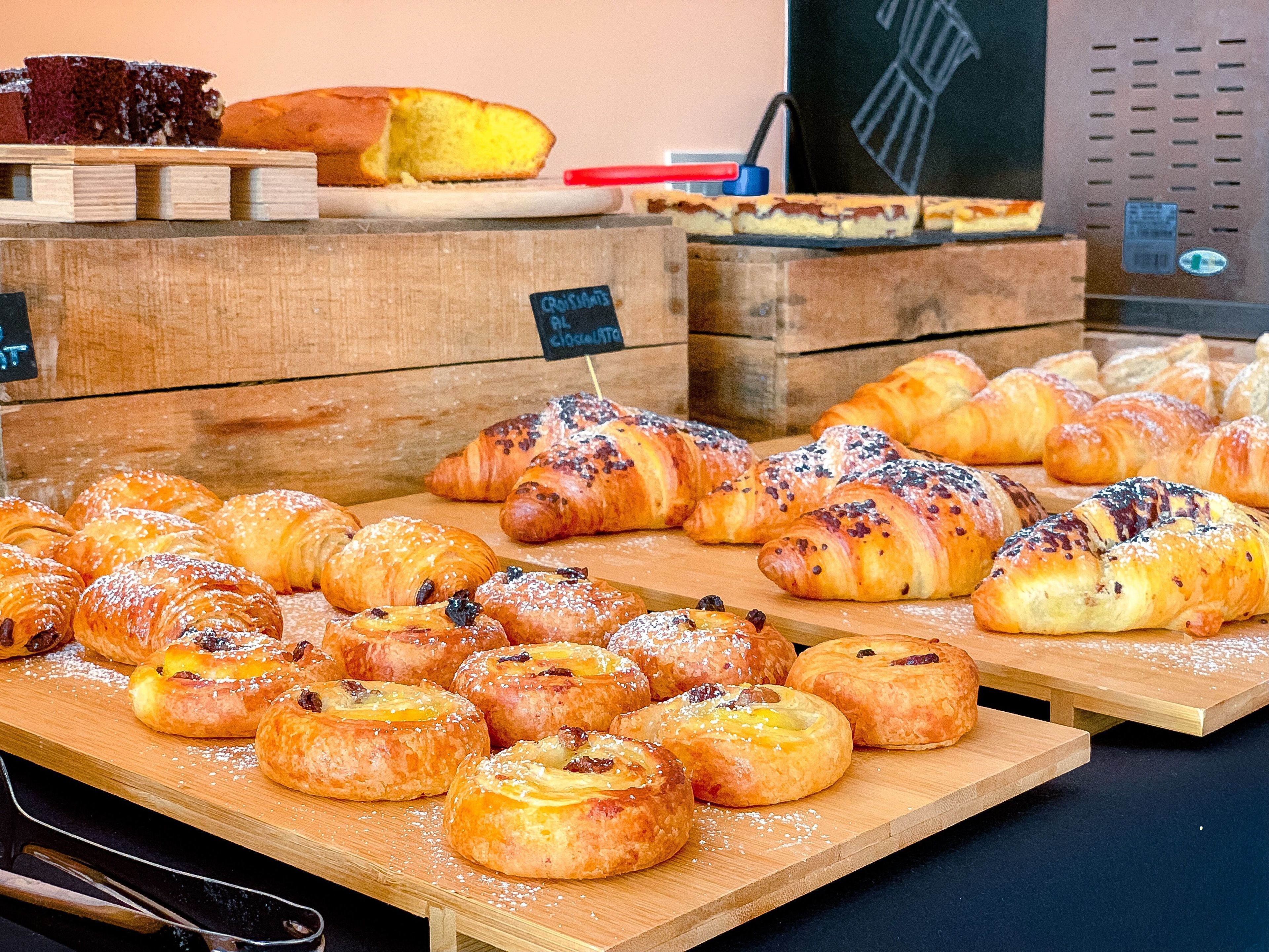 Una selezione di prodotti da forno esposti su assi di legno, tra cui pasticcini e pane.