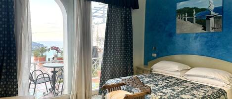 A bedroom with a bed, a chair, a painting, and a view of the outdoors.