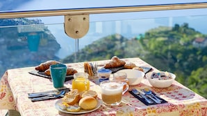 Une table dressée avec des aliments pour le petit-déjeuner, offrant une vue panoramique sur la côte.