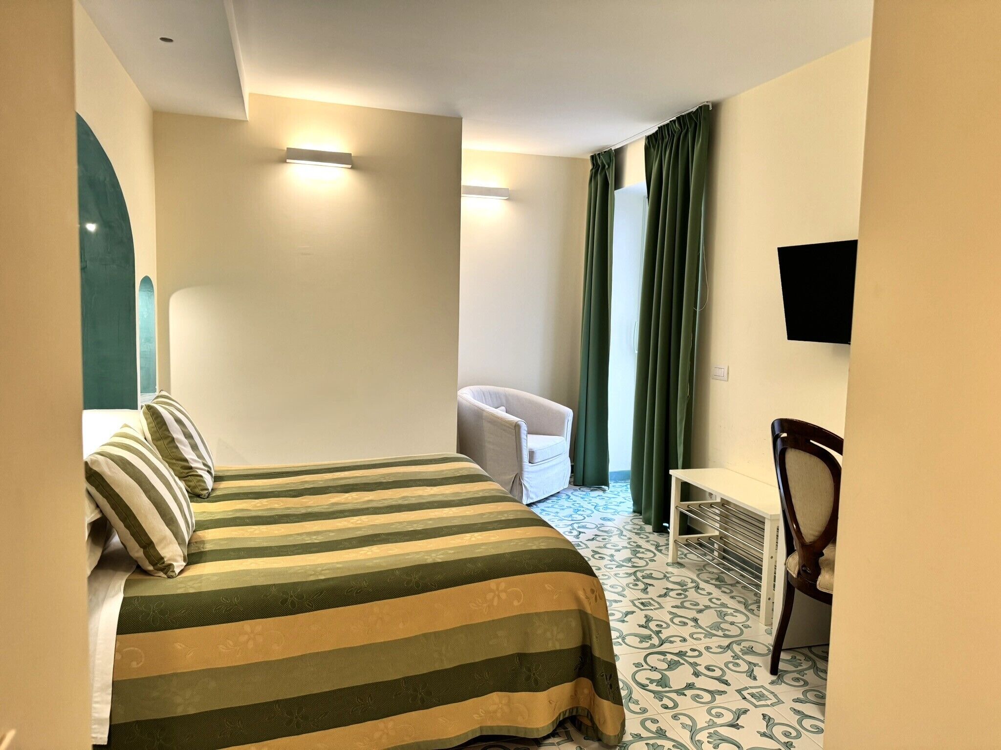Ein Hotelzimmer mit einem Bett, einem Sessel, einem Schreibtisch und einem an der Wand befestigten Fernseher.