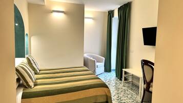 Ein Hotelzimmer mit einem Bett, einem Sessel, einem Schreibtisch und einem an der Wand befestigten Fernseher.