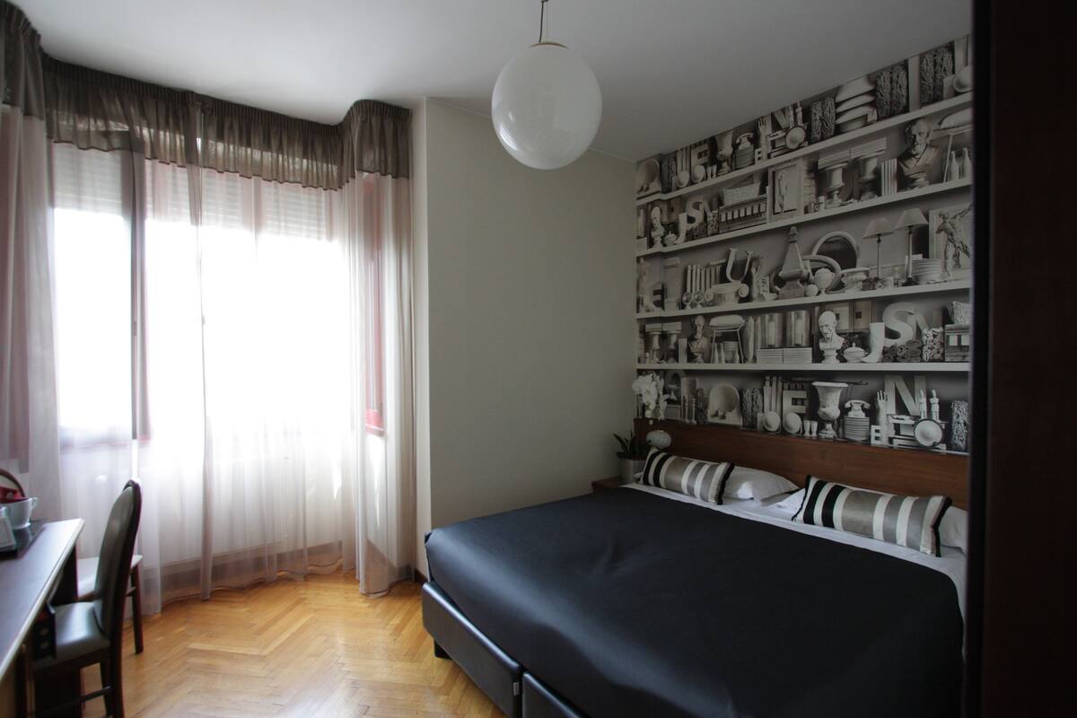 A bedroom with a bed, a desk, and a large wall of decorative items.