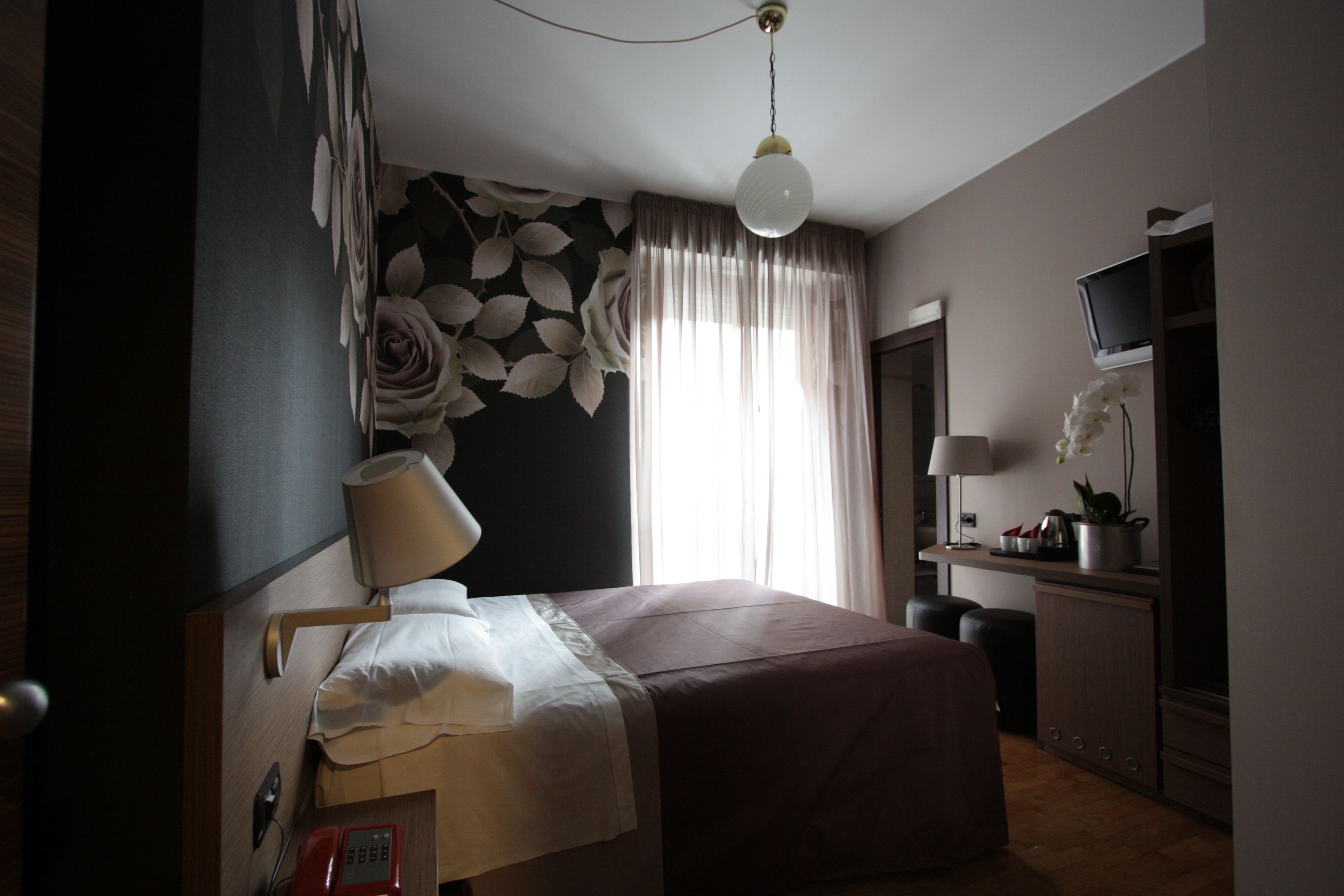 Ein Hotelzimmer mit Bett, Schreibtisch, Lampe, Fernseher und einem Fenster mit Vorhängen.