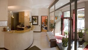 Een moderne receptie met een gebogen balie, een zithoek met een gestreept bankje en een glazen deur naar buiten.