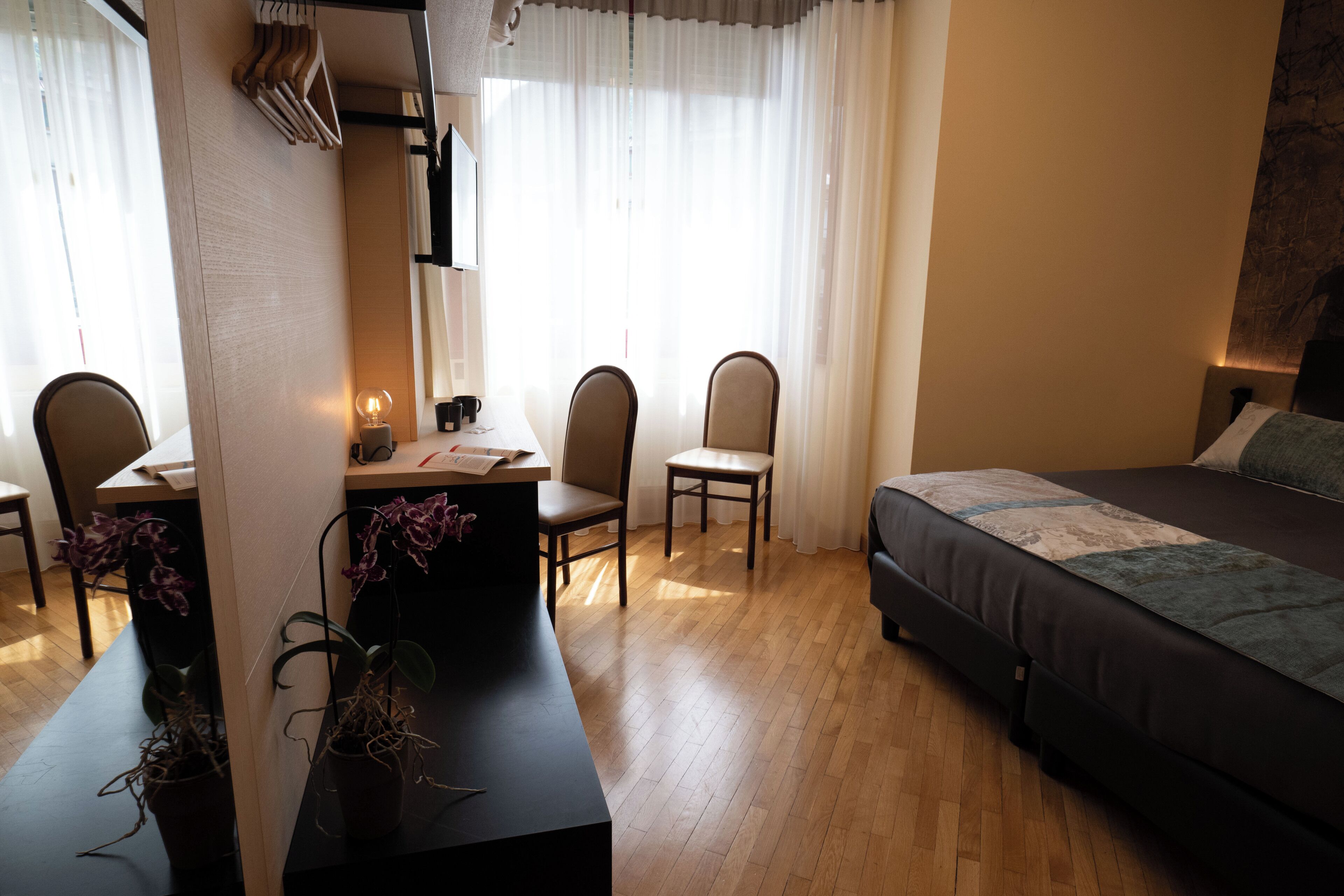 Una habitación de hotel con una cama, dos sillas, un escritorio, una lámpara y una planta en maceta.