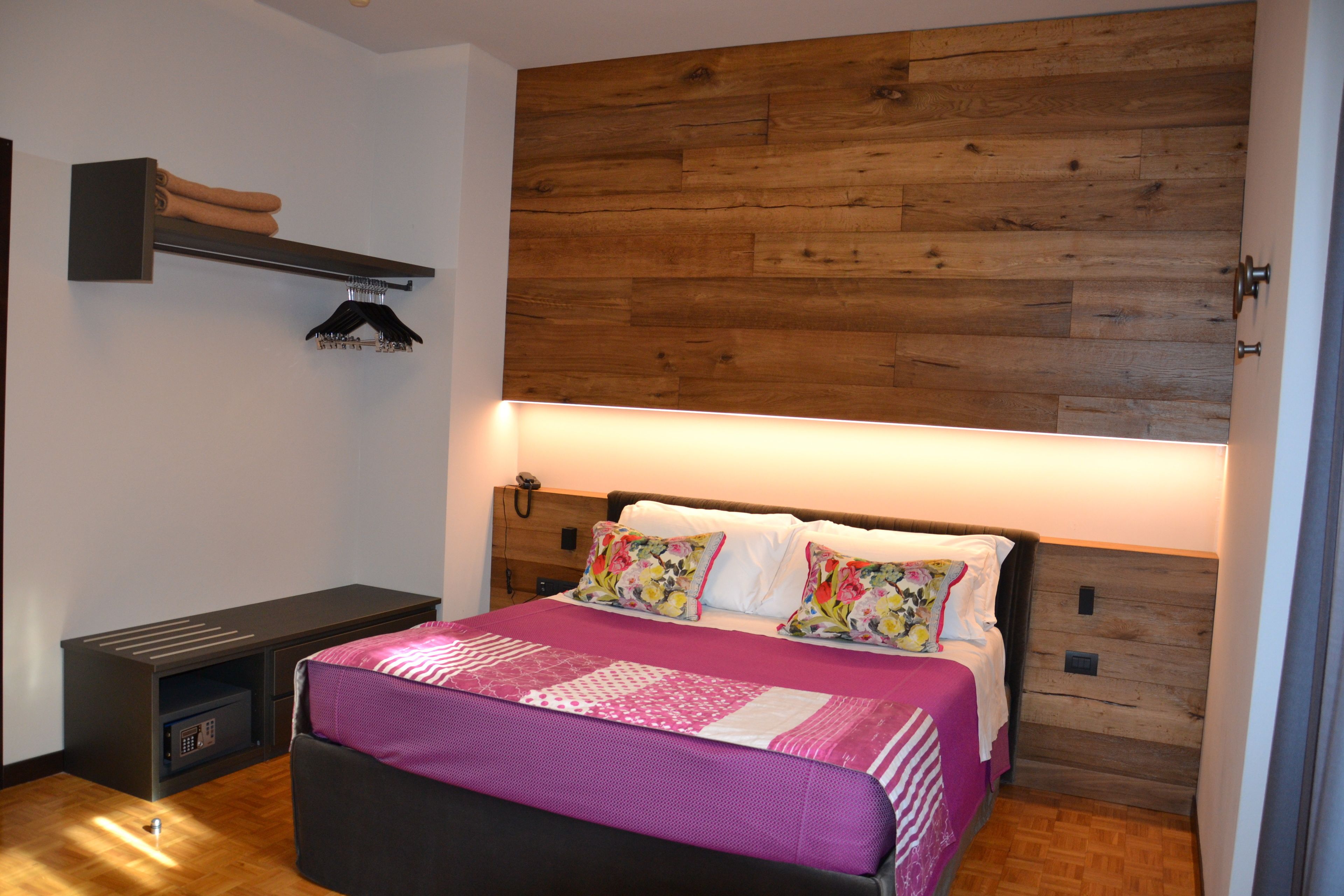 A bedroom with a wooden headboard, a bed with floral pillows, a bedside table, and a bench.