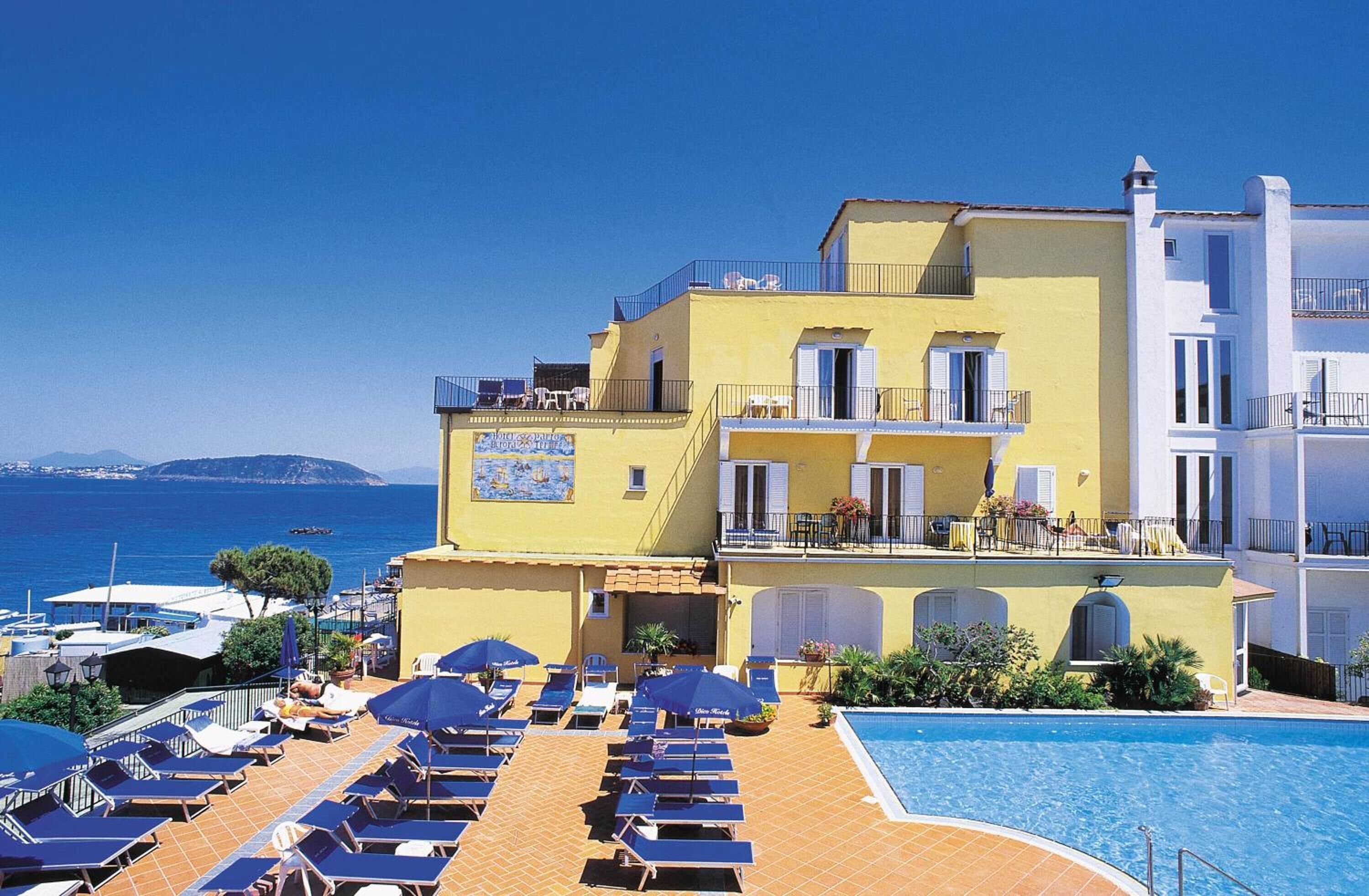 A hotel with a pool area, sun loungers, and a view of the sea.