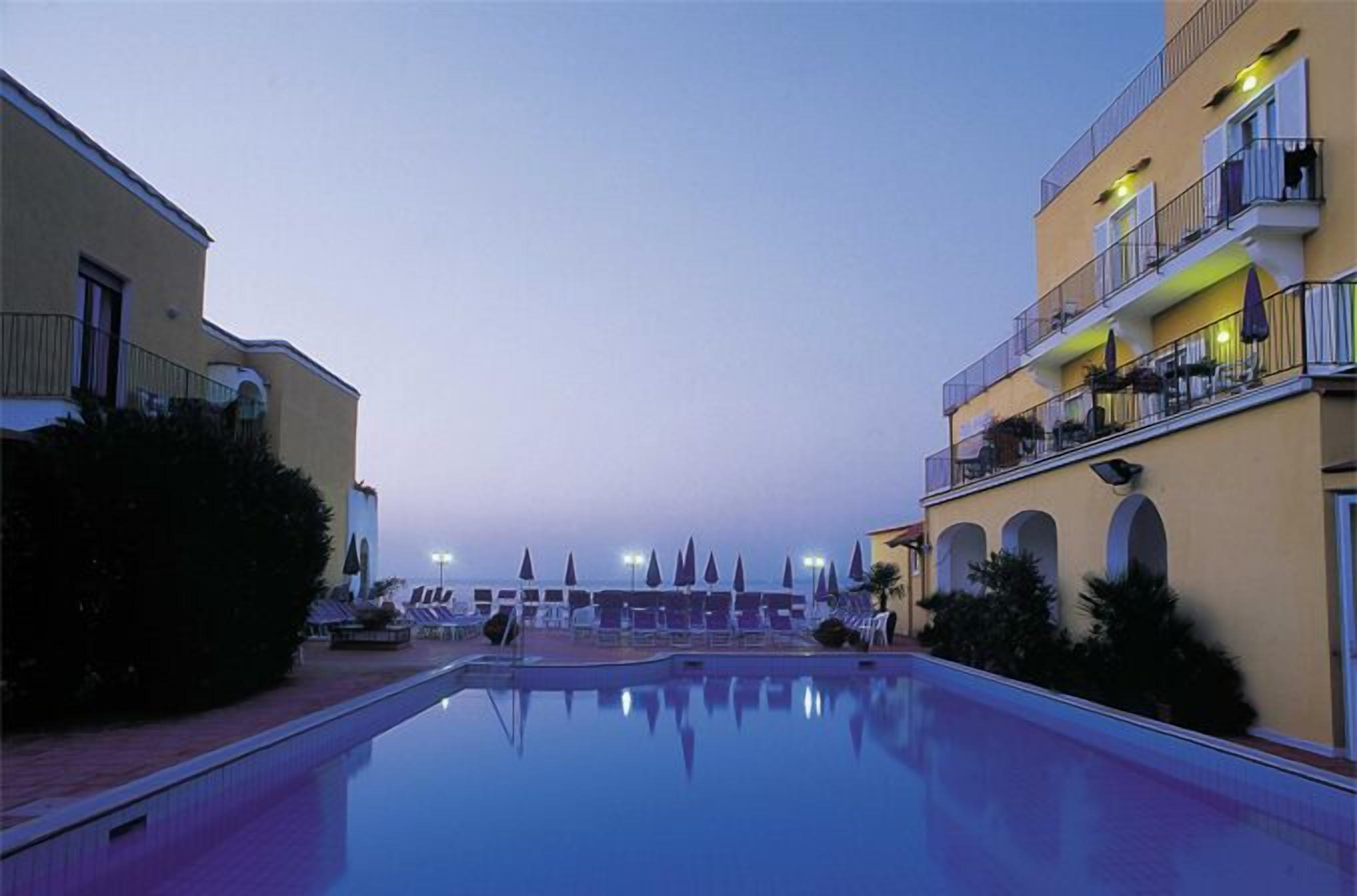 A pool area with lounge chairs and umbrellas, surrounded by buildings with balconies and arched windows.