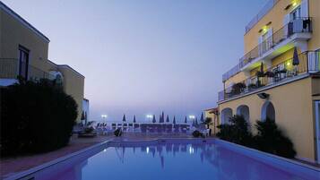 A pool area with lounge chairs and umbrellas, surrounded by buildings with balconies and arched windows.