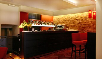 Un área de bar moderna con una pared de piedra, una variedad de botellas de licor, una máquina de café y taburetes rojos.