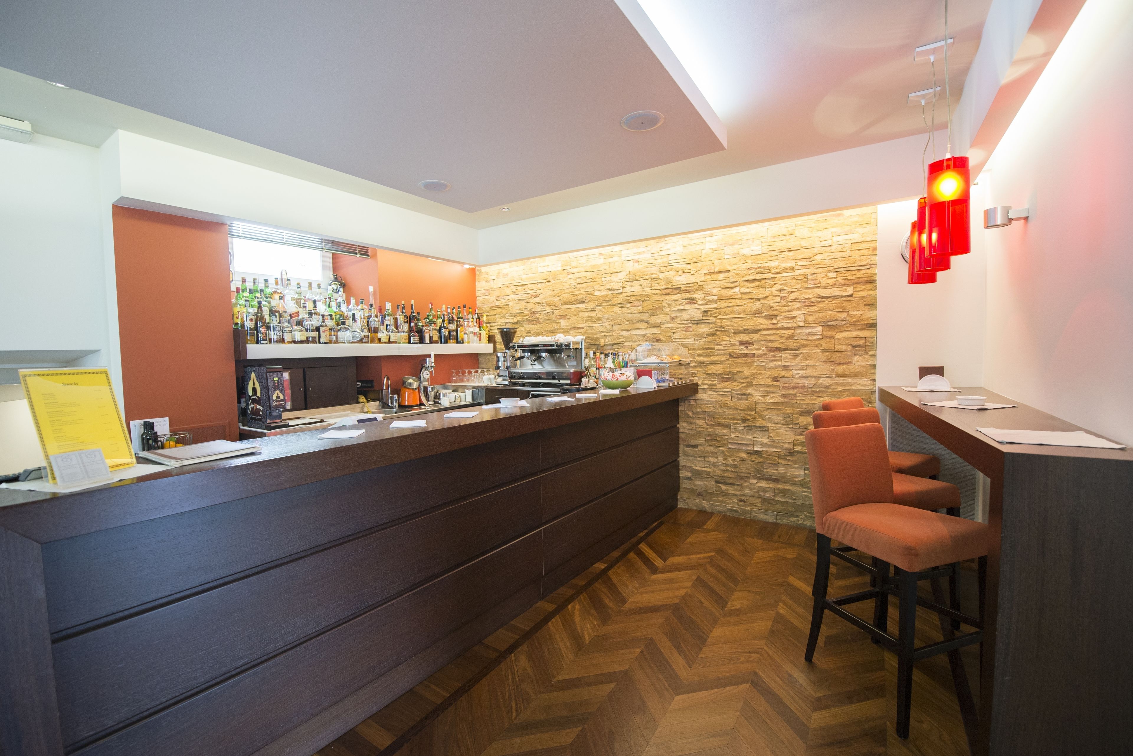 A bar area with a wooden herringbone floor, a stone accent wall, and a counter with various bottles and a coffee machine.