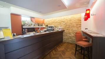 A bar area with a wooden herringbone floor, a stone accent wall, and a counter with various bottles and a coffee machine.