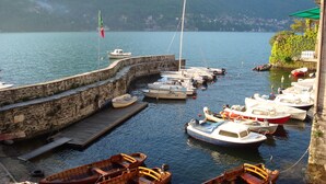 A marina with various boats docked, a stone wall, and a mountainous backdrop. - Hotel Posta (Moltrasio)