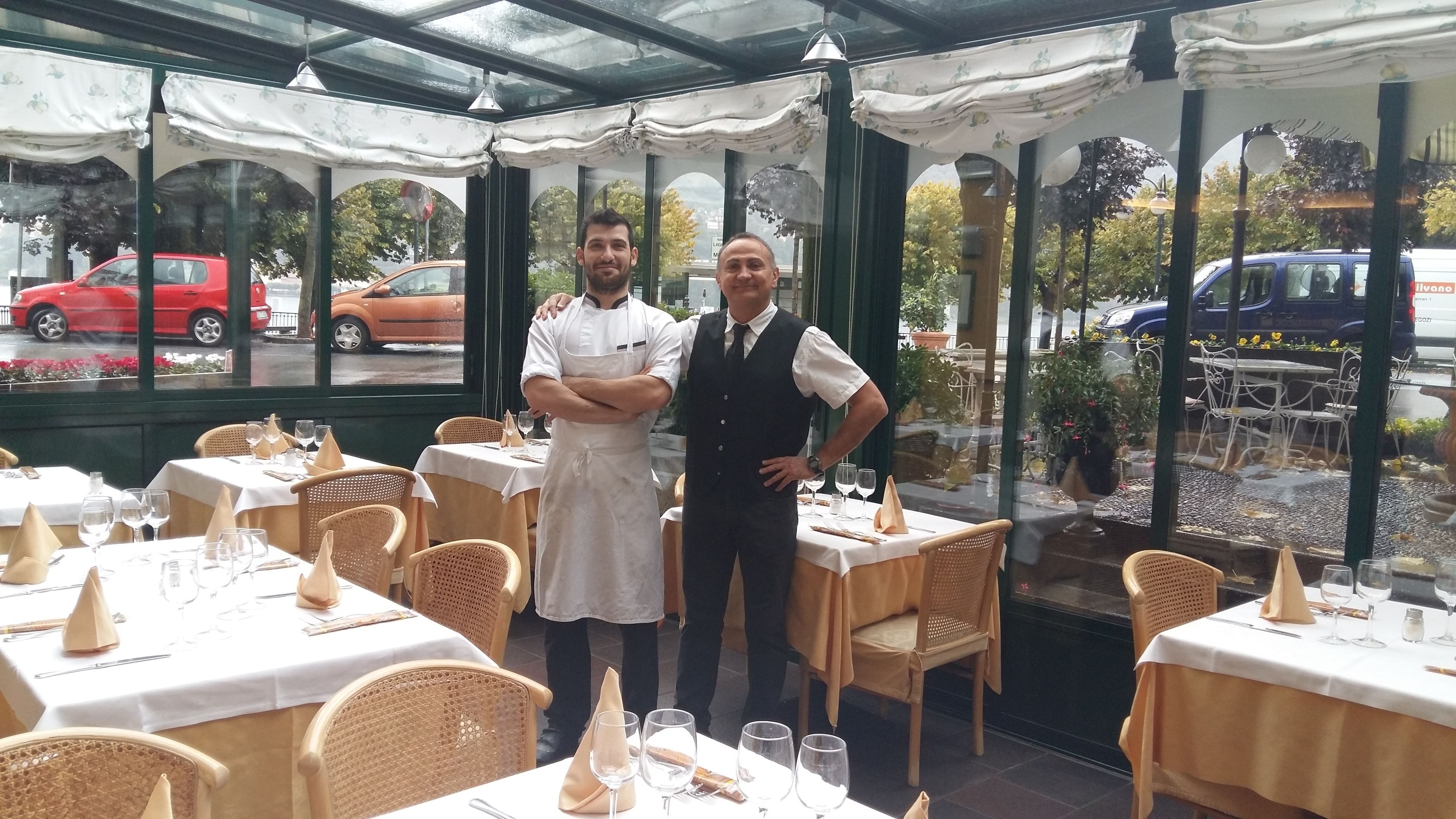 A restaurant with tables set for dining, a glass-enclosed patio, and a view of the street.
