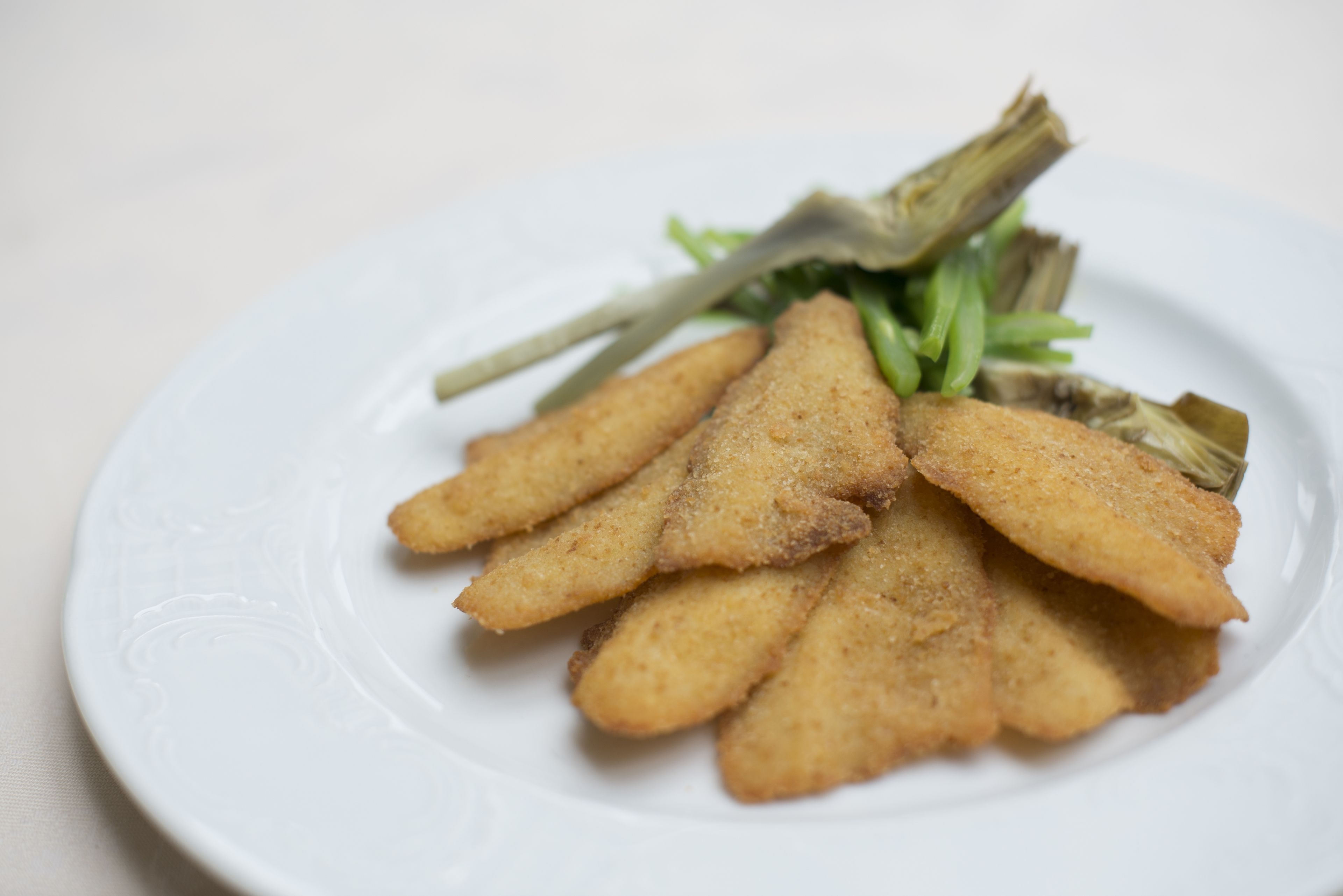 A white plate with triangular-shaped fried food items and some green vegetables.
