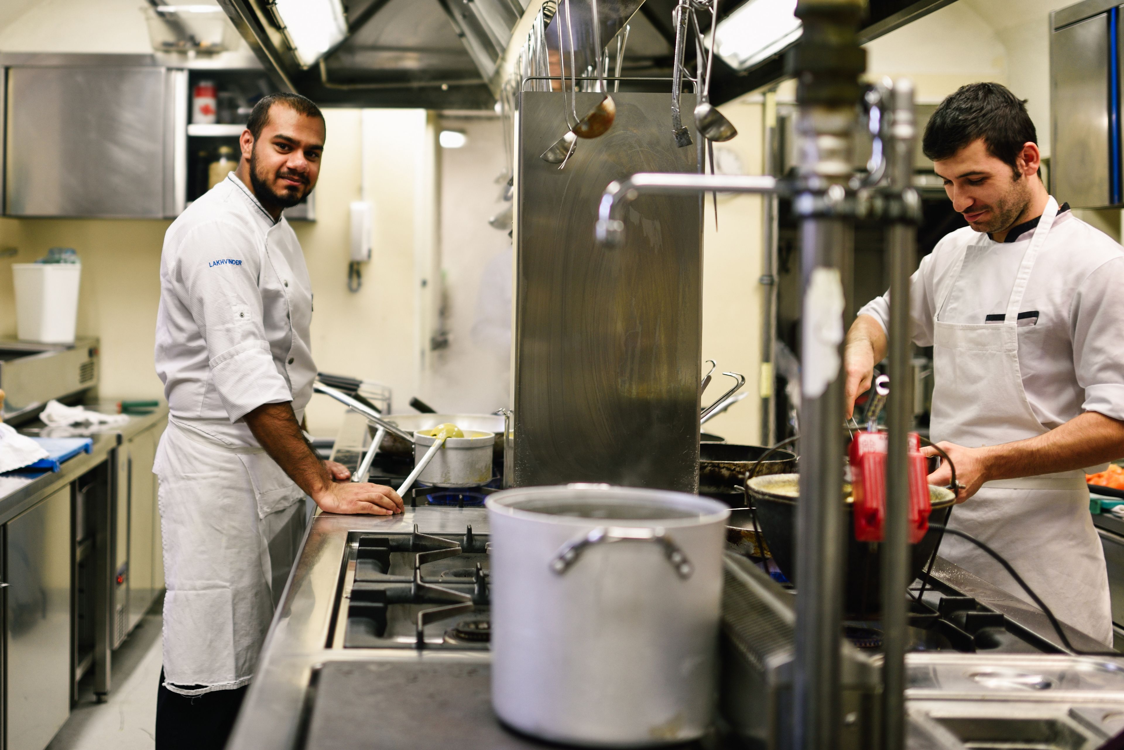 Uma cozinha profissional com eletrodomésticos de aço inoxidável e chefs de uniforme branco.