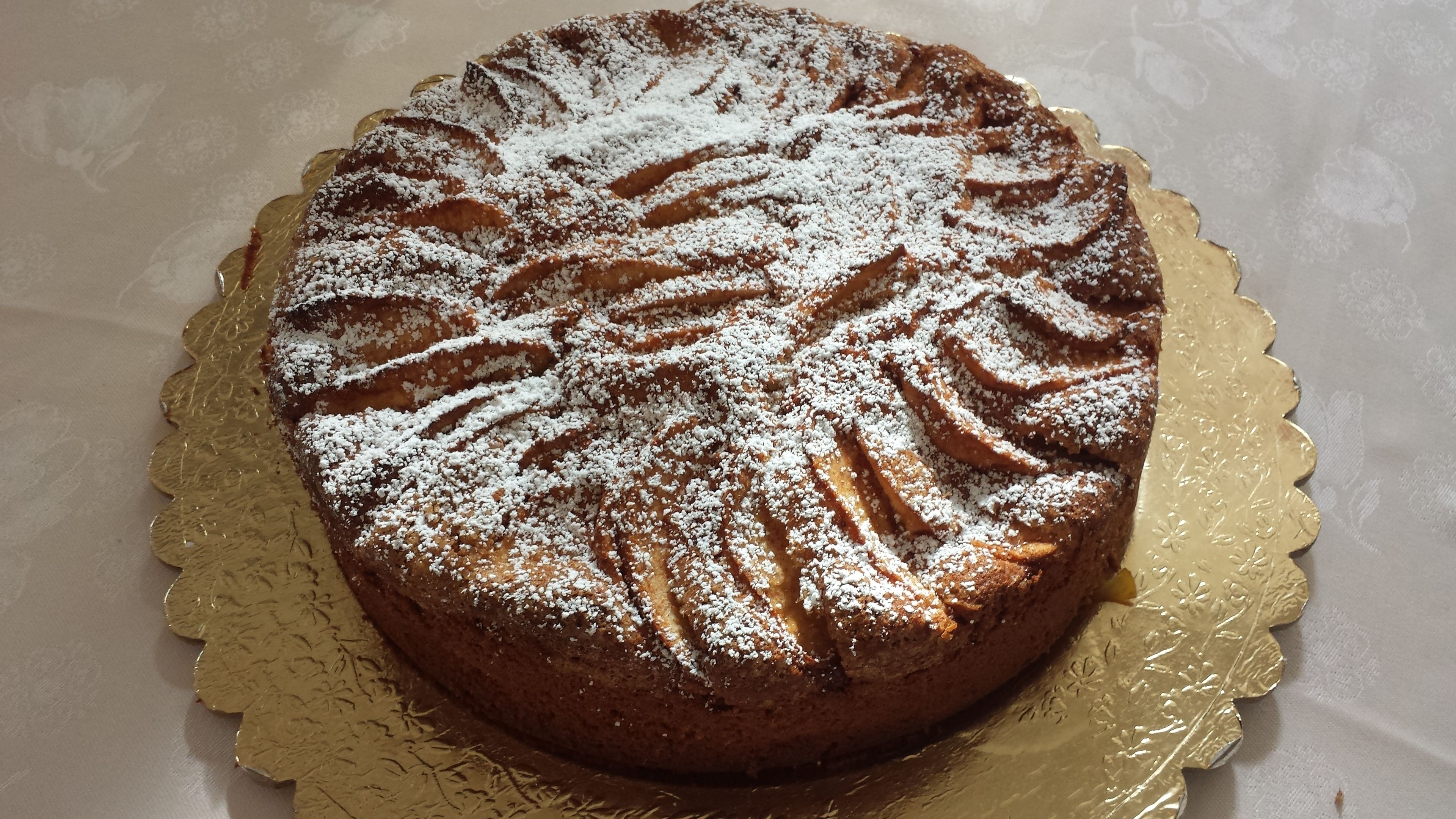 Ein runder Kuchen mit Puderzucker auf einer goldenen Kuchenplatte.