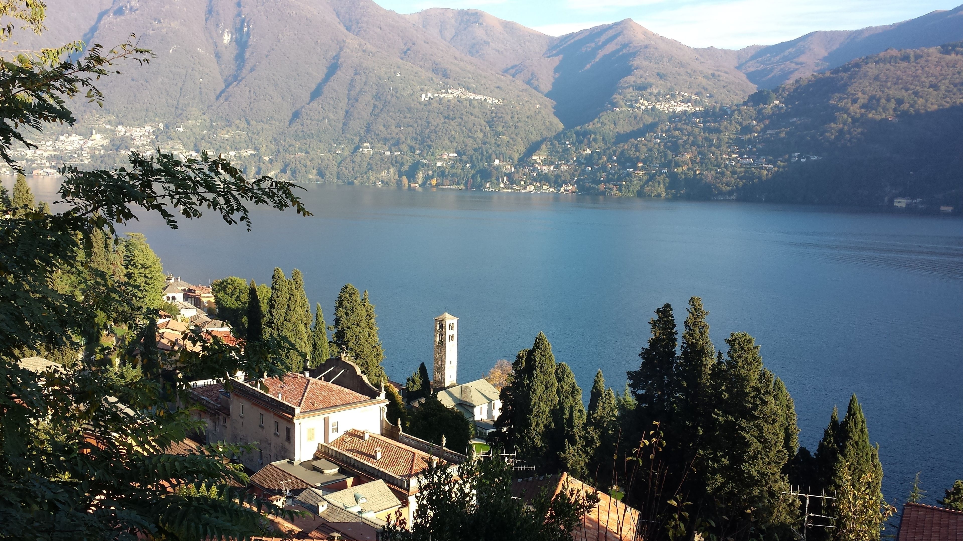 Un village au bord d’un lac, doté d’une architecture traditionnelle, d’un clocher d’église imposant et surplombé par des montagnes.