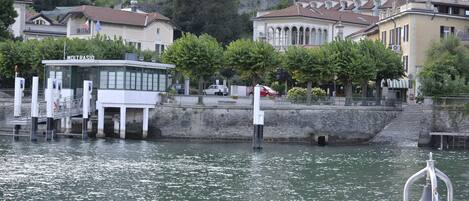 Un edificio frente al agua con un muelle, una bandera y una campana.