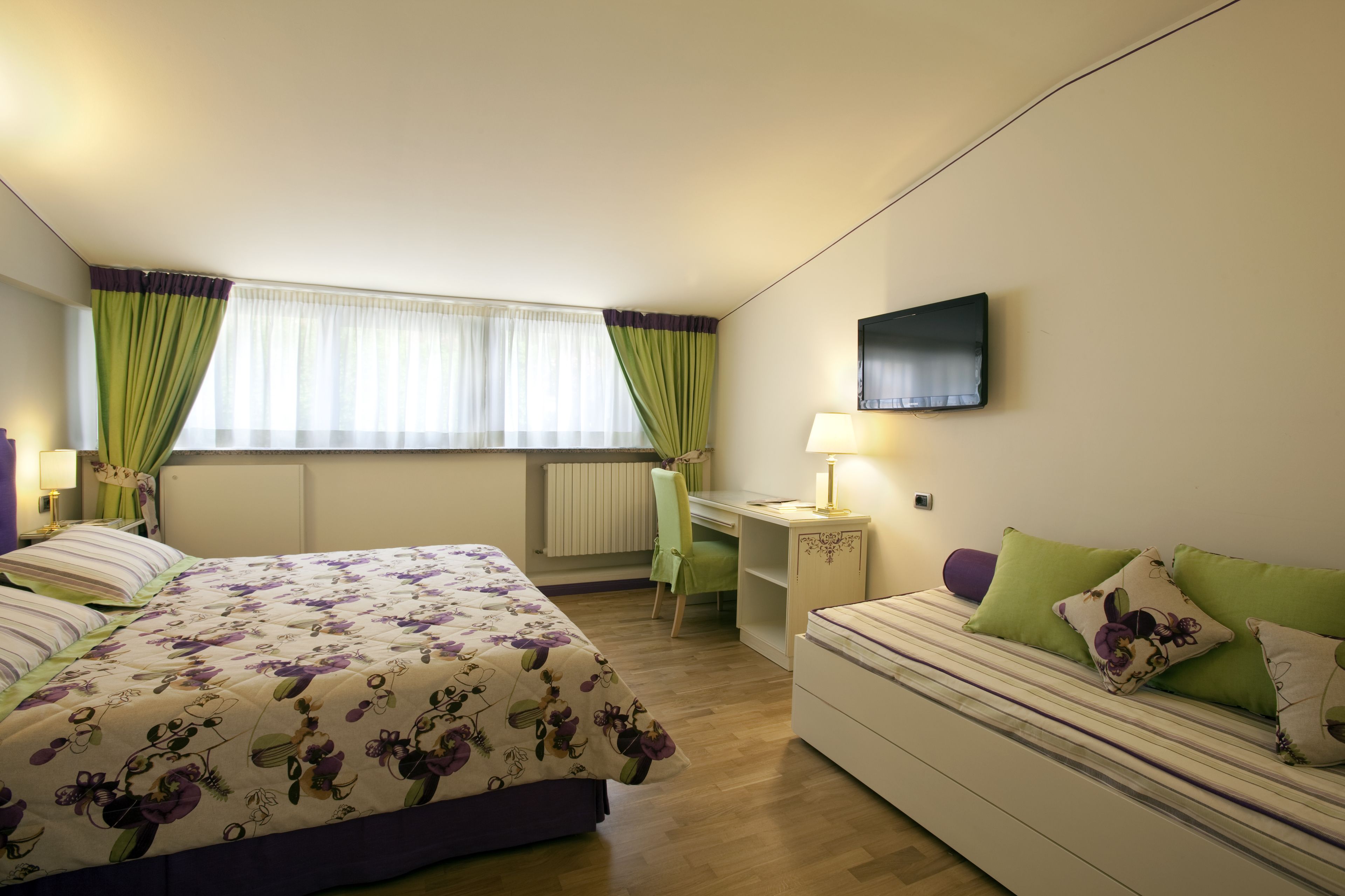 A bedroom with a bed, a desk, a chair, and a TV.