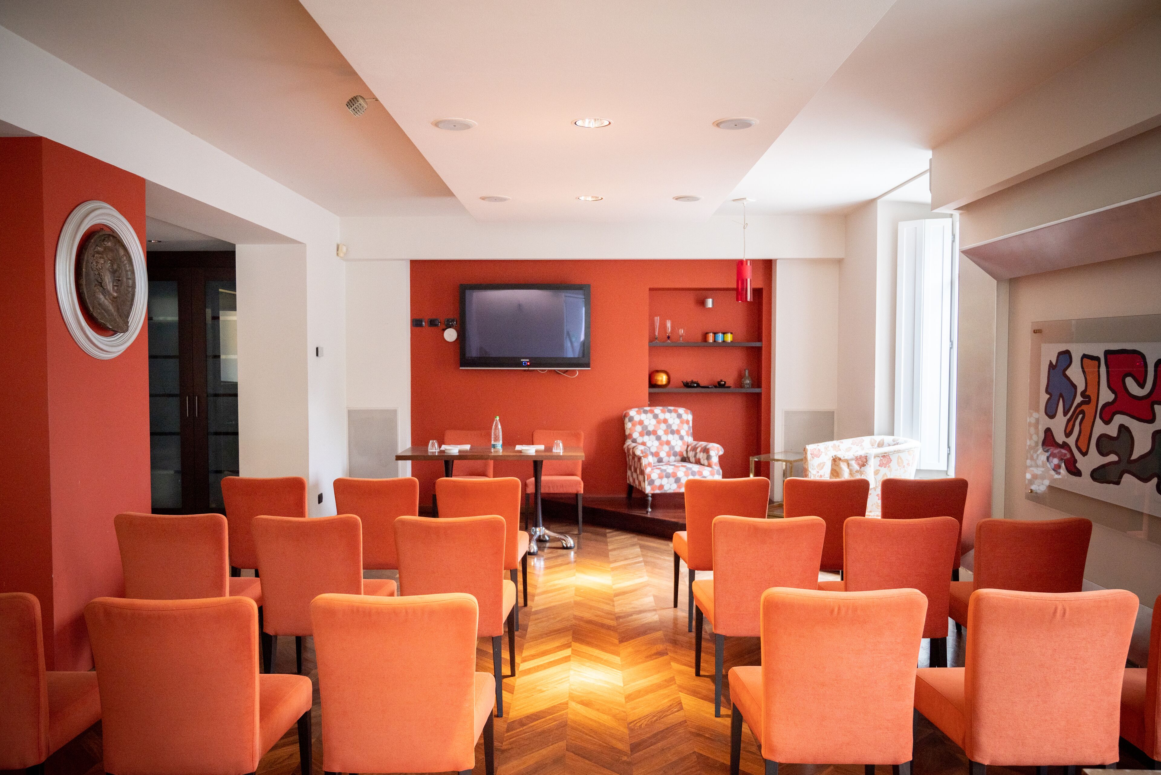 A conference room with orange chairs, a television, and a red accent wall.