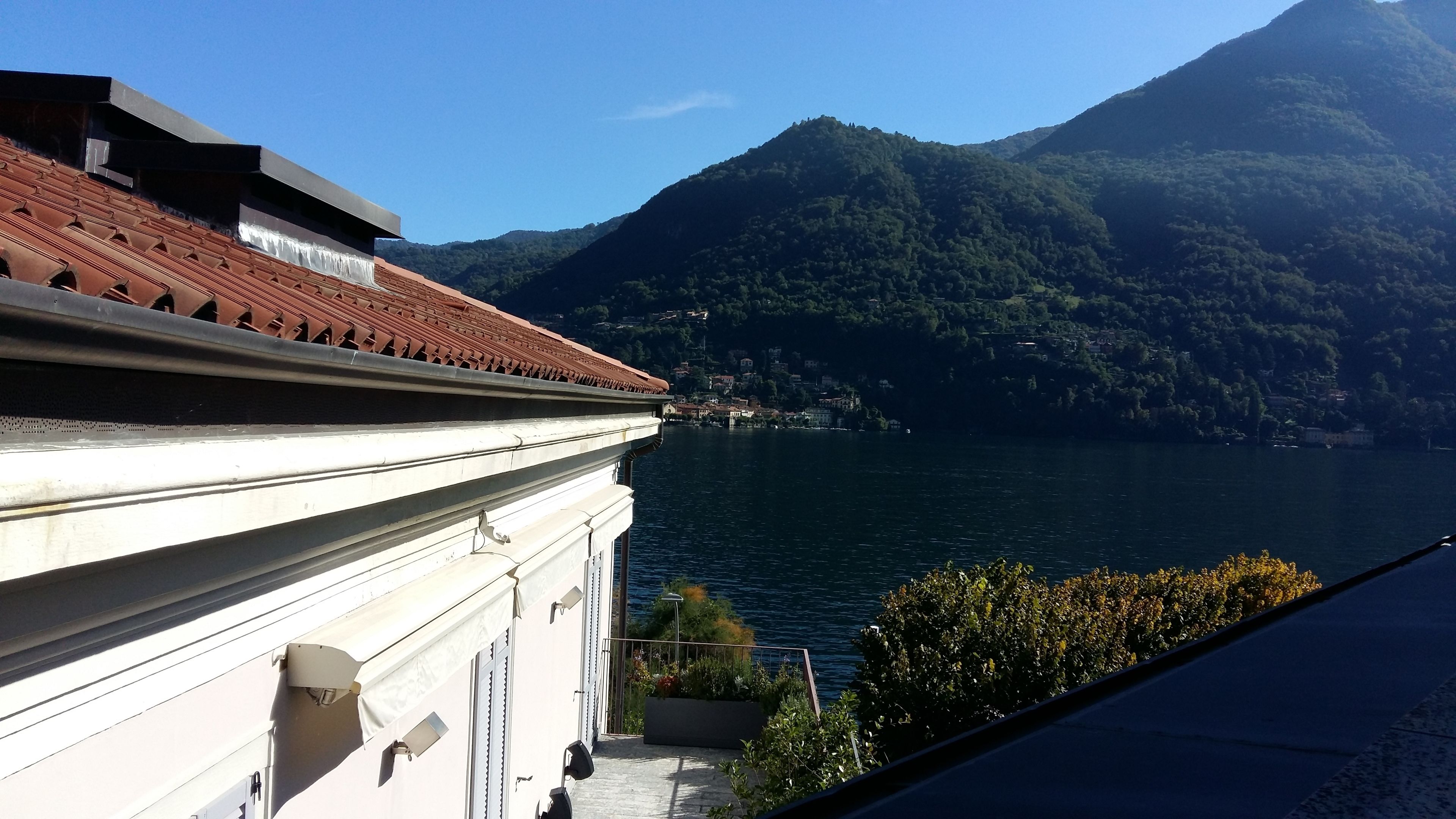 A building with a red-tiled roof overlooking a lake and mountains.