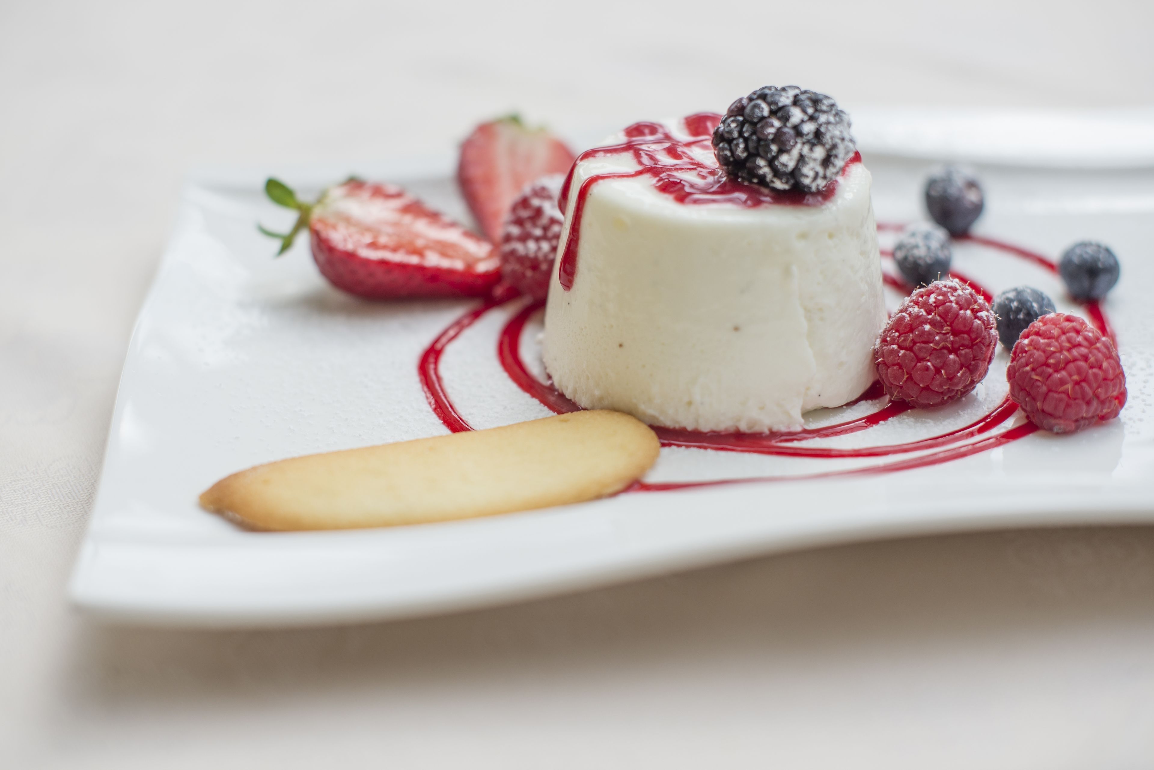 Un postre con frutos rojos y una galleta sobre un plato blanco.