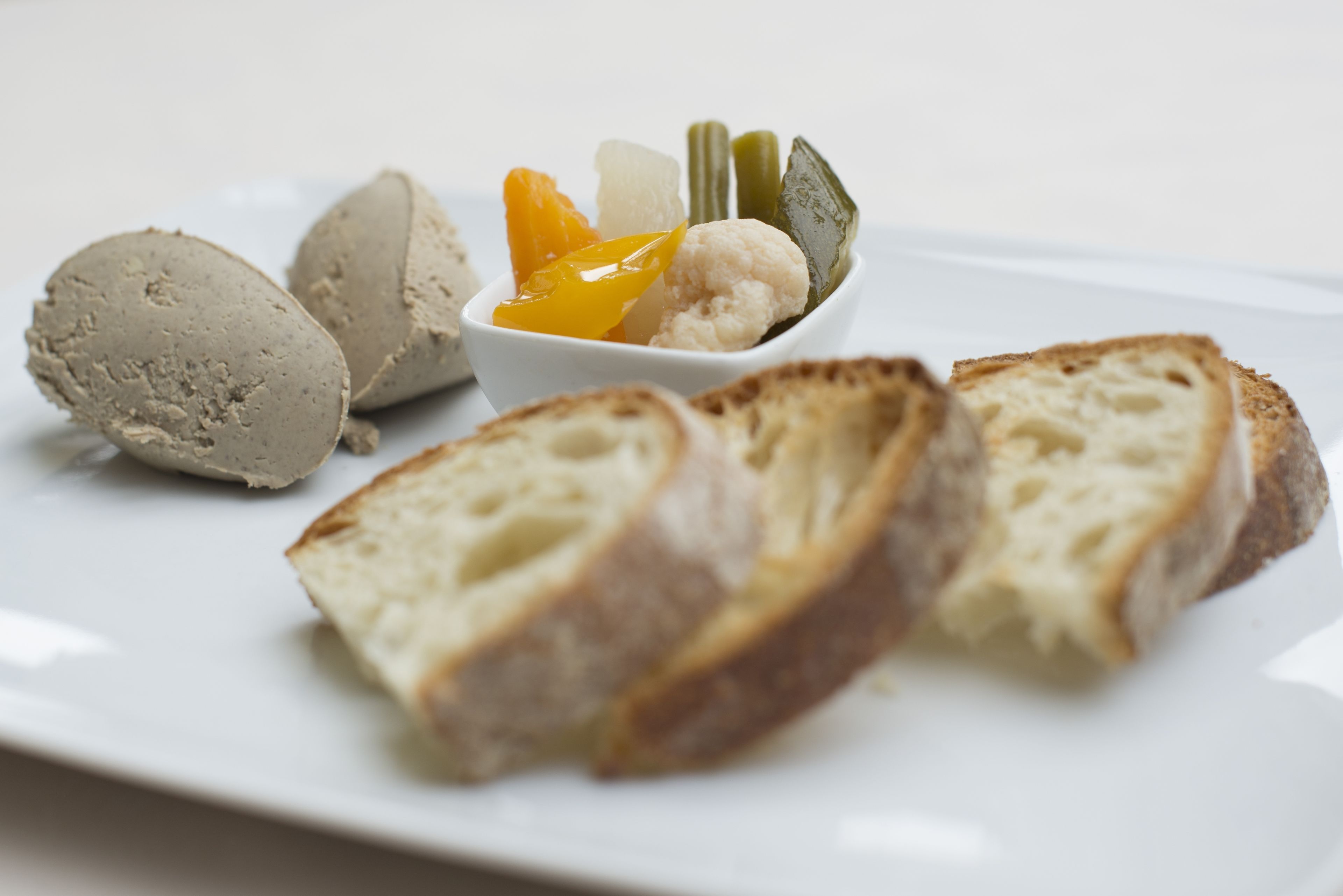 A plate with slices of bread and a small bowl containing various pickles and a yellow pepper.