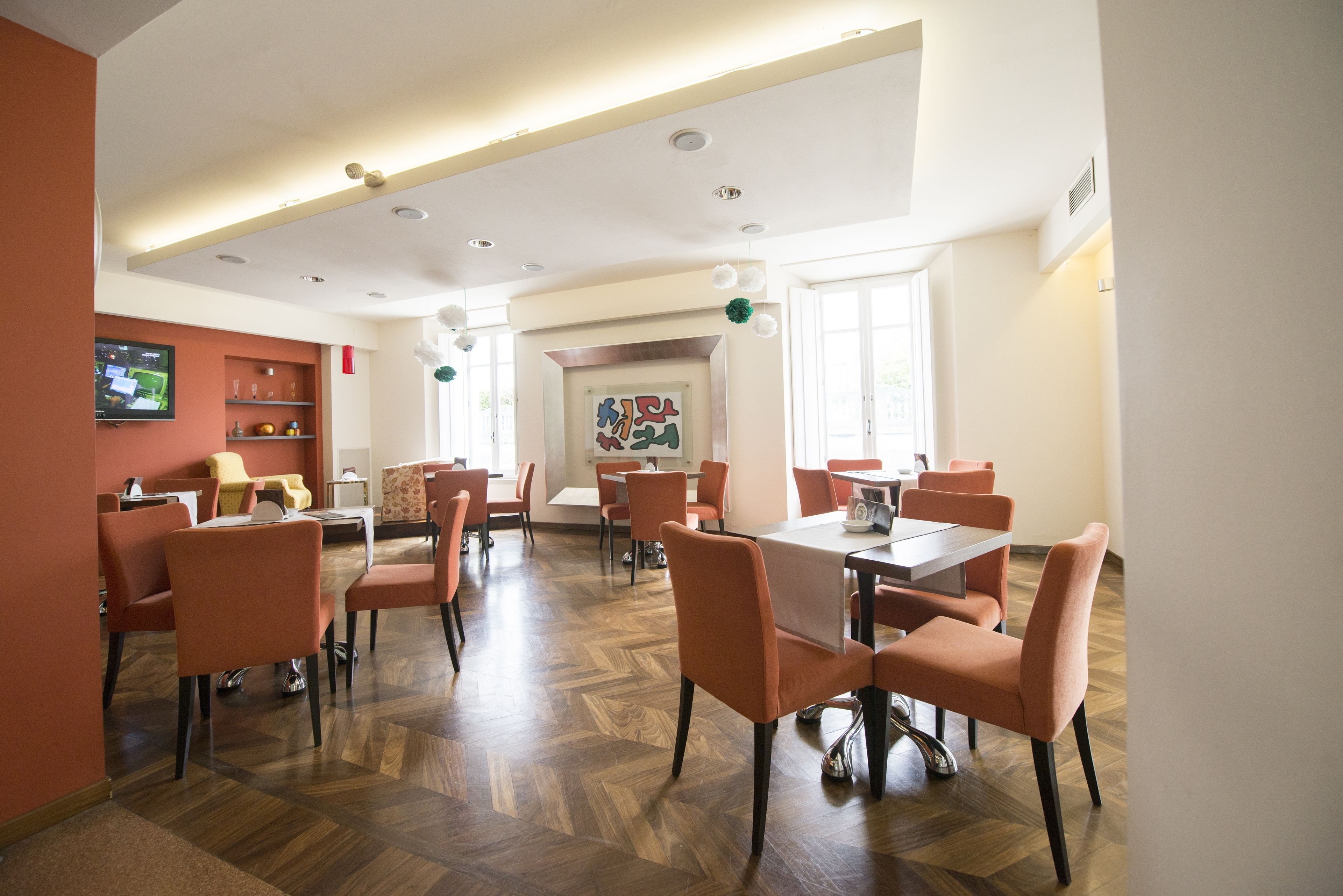 A spacious dining area with multiple tables and chairs, a television on the wall, and a decorative painting on the wall.
