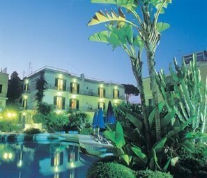 A hotel with a swimming pool, surrounded by lush greenery and palm trees. - Hotel Royal Terme (Ischia)
