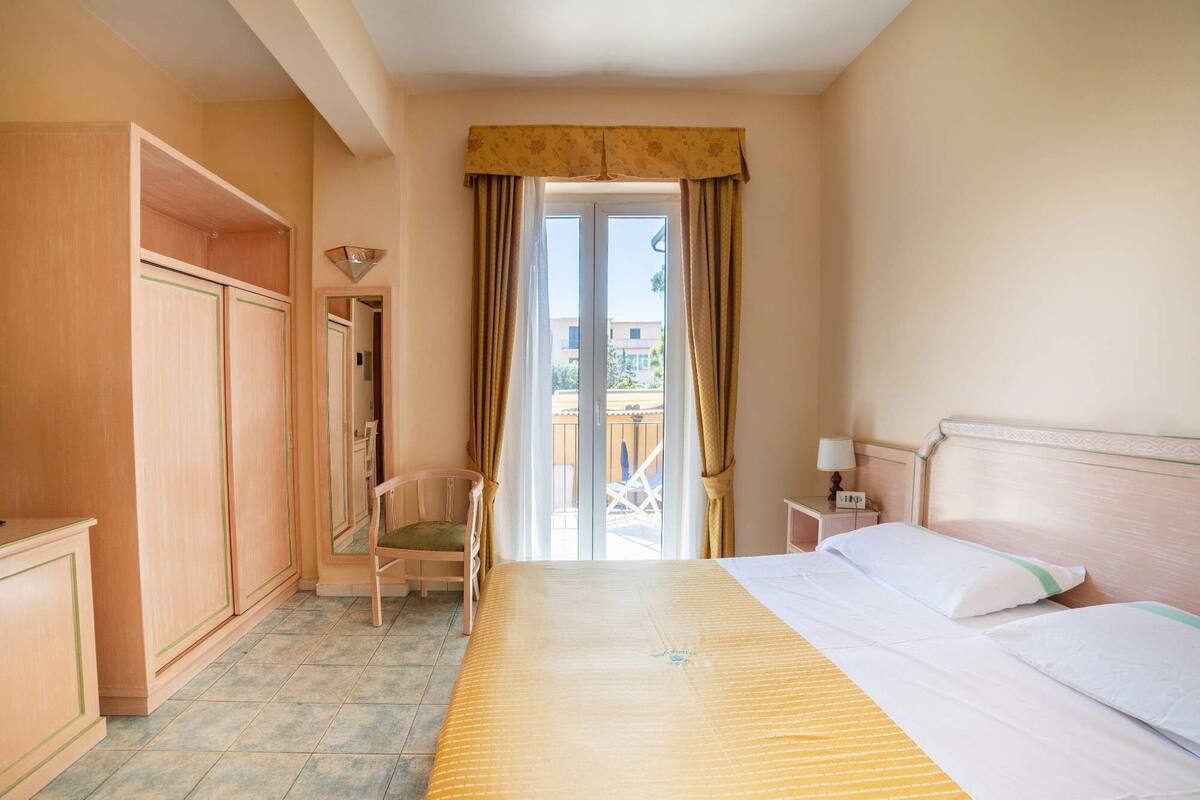 A hotel room with a bed, a chair, a desk, and a wardrobe.