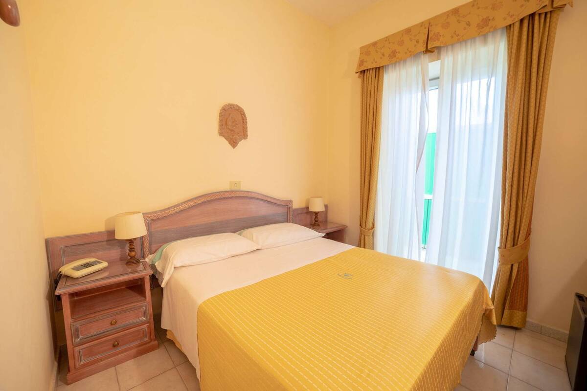 A hotel room with a bed, bedside tables, a telephone, and curtains.