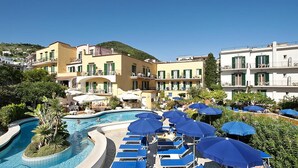 Un resort con piscina rodeada de sillas de descanso azules y sombrillas, y edificios con balcones.