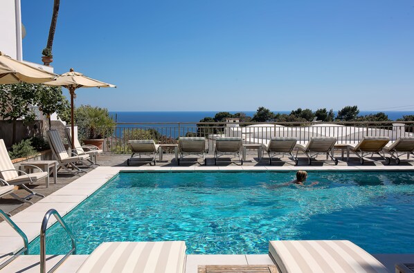 Una piscina al aire libre, sombrillas, sillones reclinables de piscina