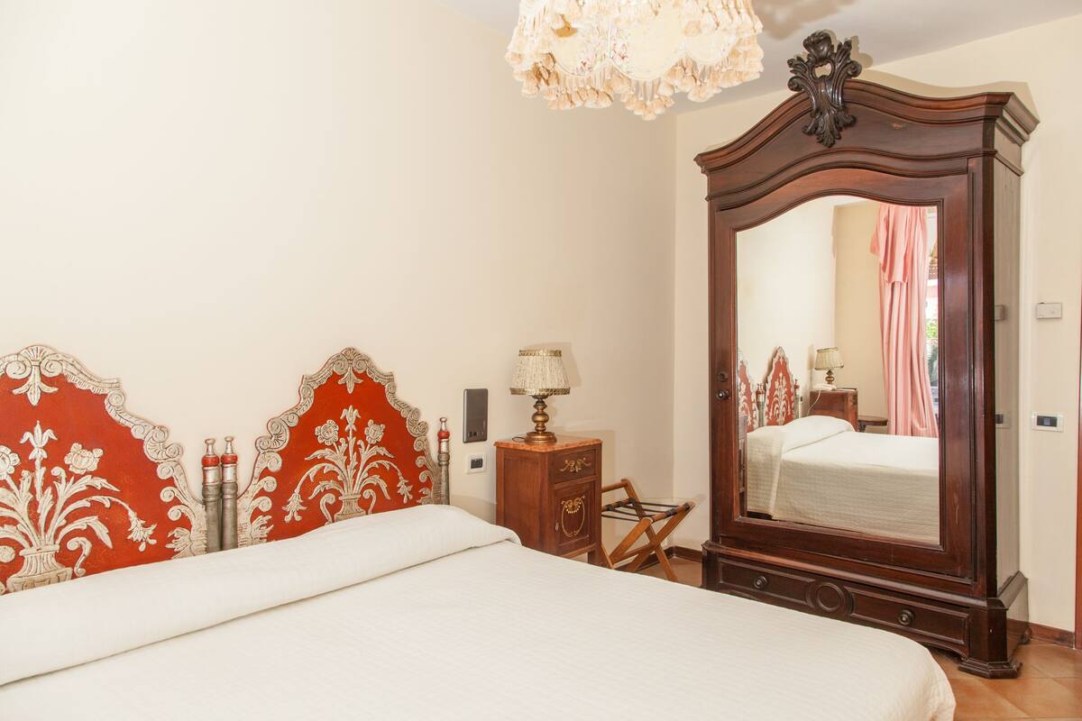 A bedroom with a large mirror, a bed, a nightstand, and a lamp.