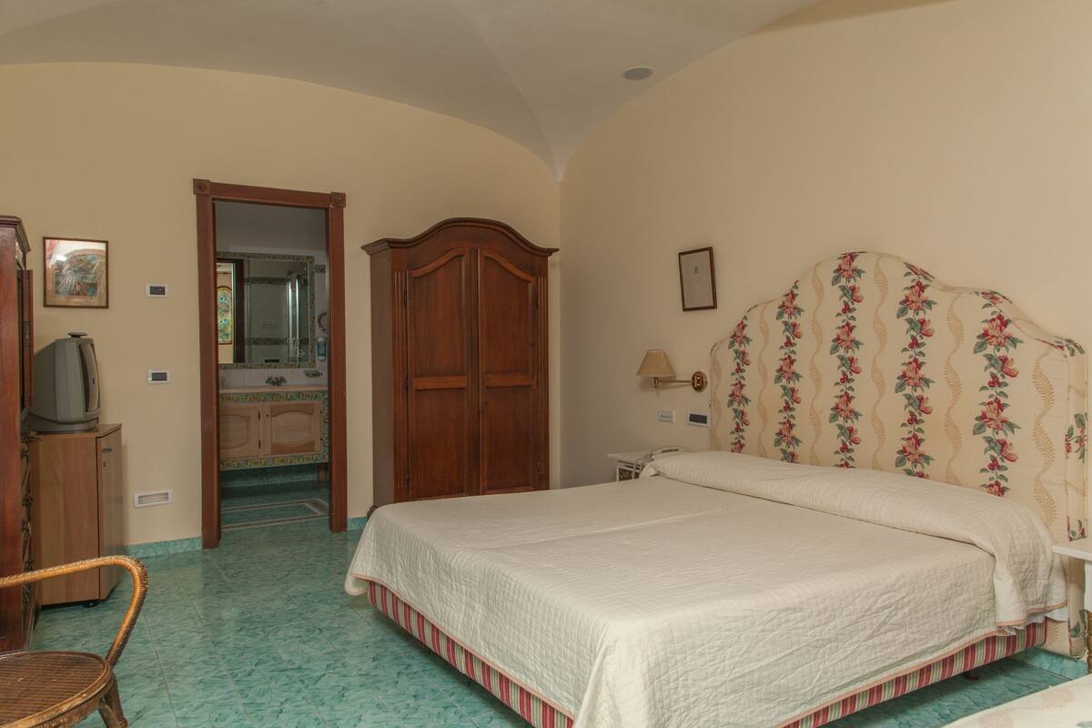 A bedroom with a bed, a wooden wardrobe, a television, and a bathroom visible through an open door.