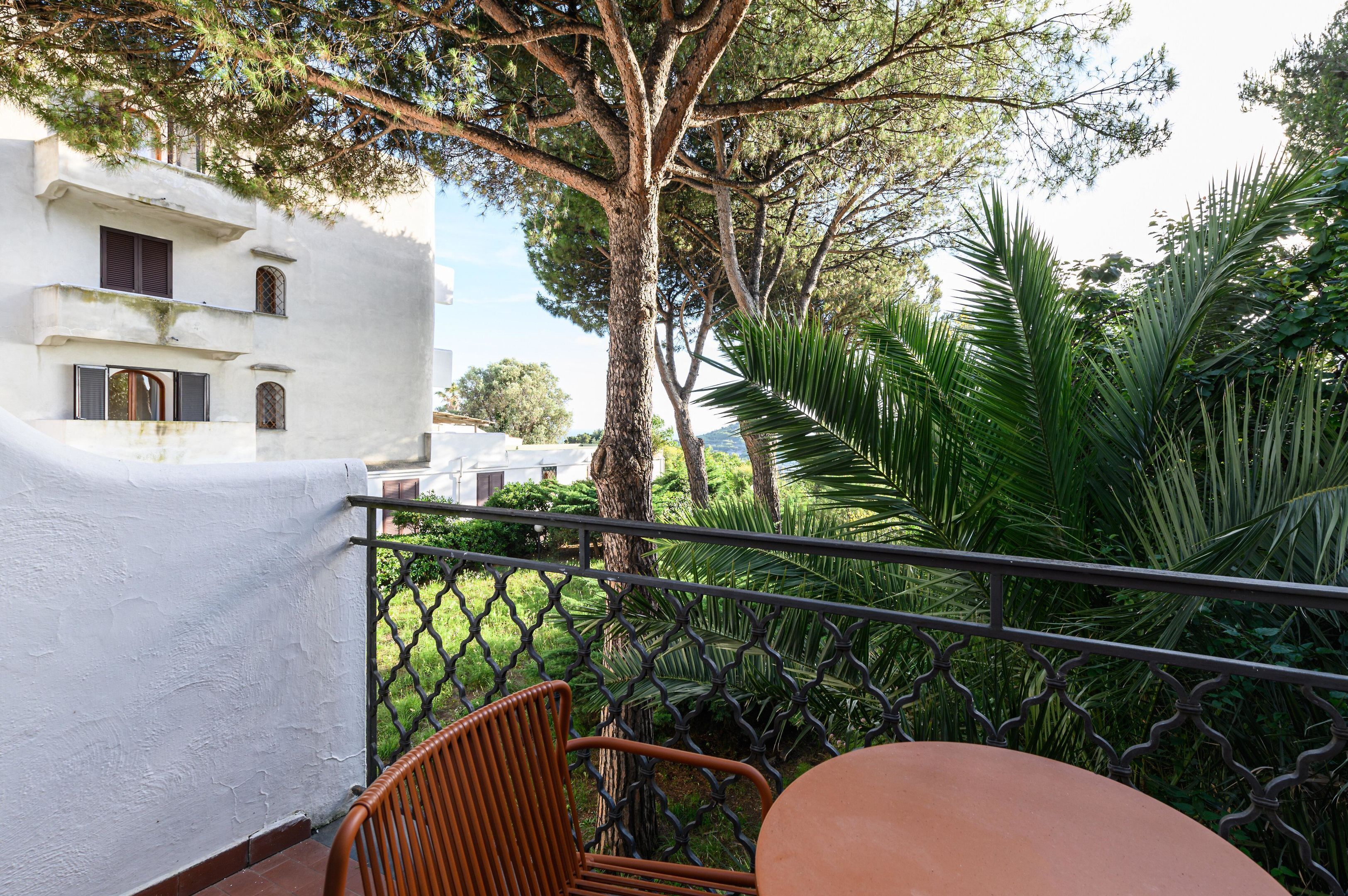 A balcony with a wrought iron railing, a terracotta table, and a wicker chair.