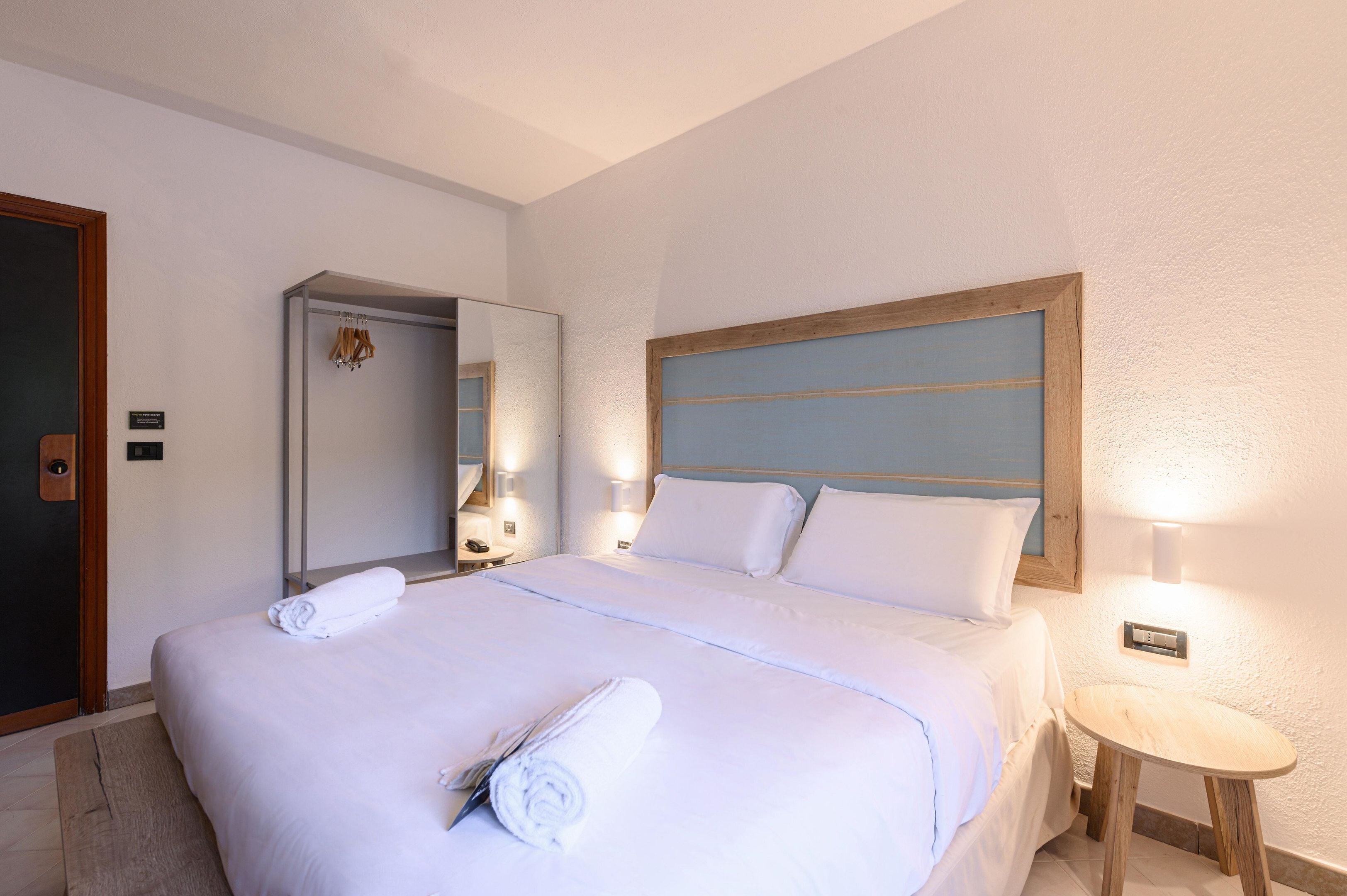A hotel room with a large bed, a wooden headboard, a bedside table, and a mirror.