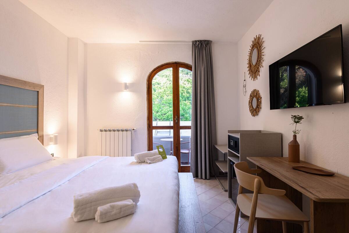 A hotel room with a bed, a desk, a chair, a TV, and a window with curtains.