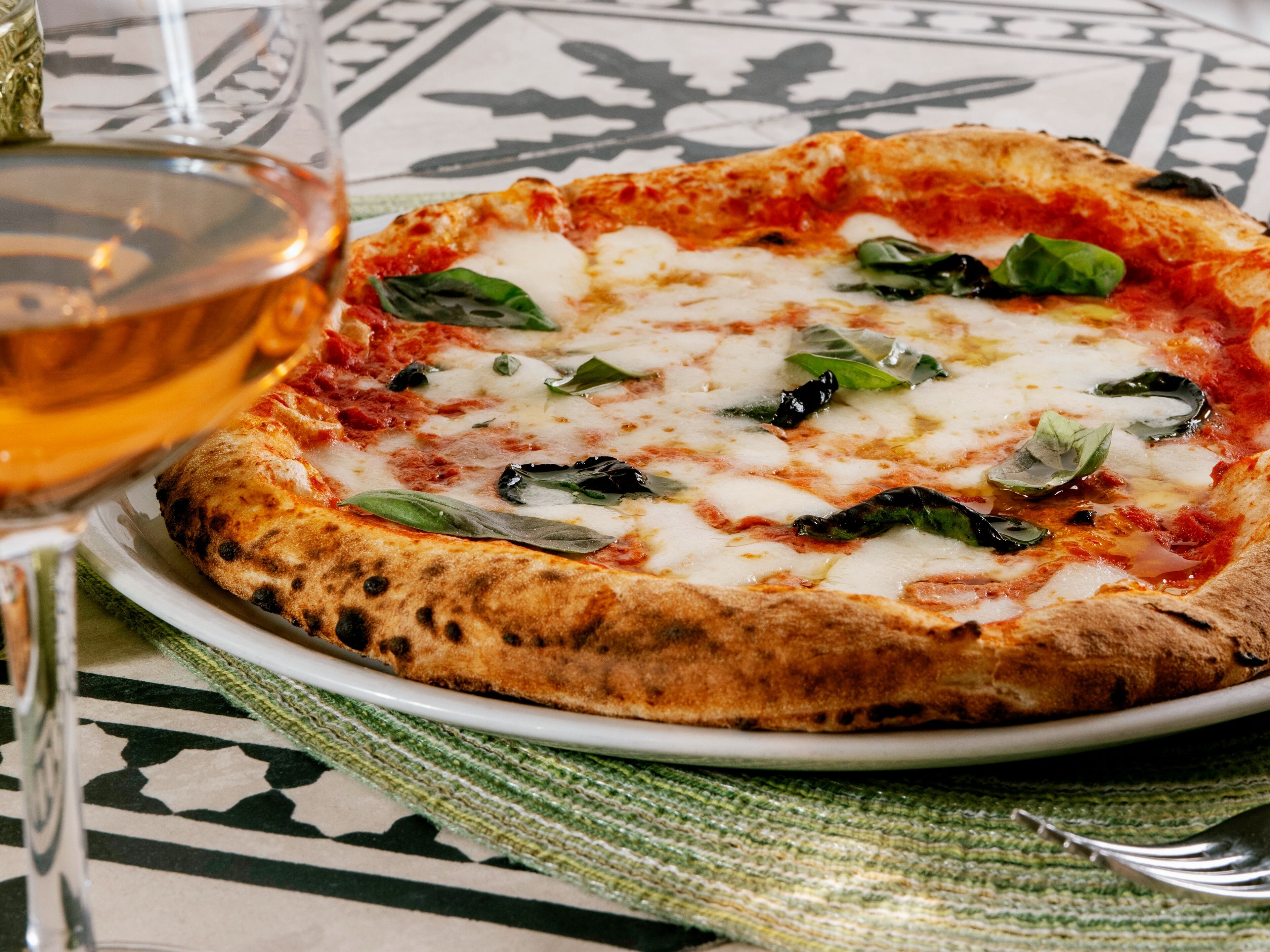 A pizza on a plate with a glass of wine beside it.
