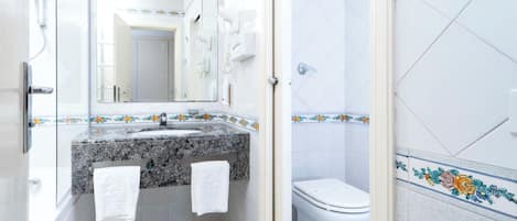 A bathroom with a granite countertop, a white sink, a mirror, a toilet, and a shower area.