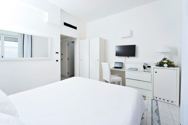 Una habitación de hotel con cama, escritorio, computadora portátil, televisor y armario.