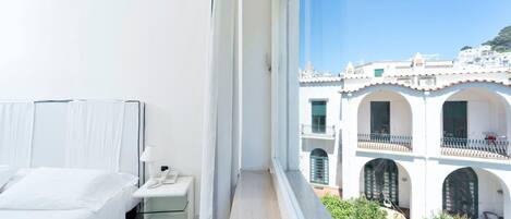 A hotel room with a bed, bedside table, and a view of a white building with arches.