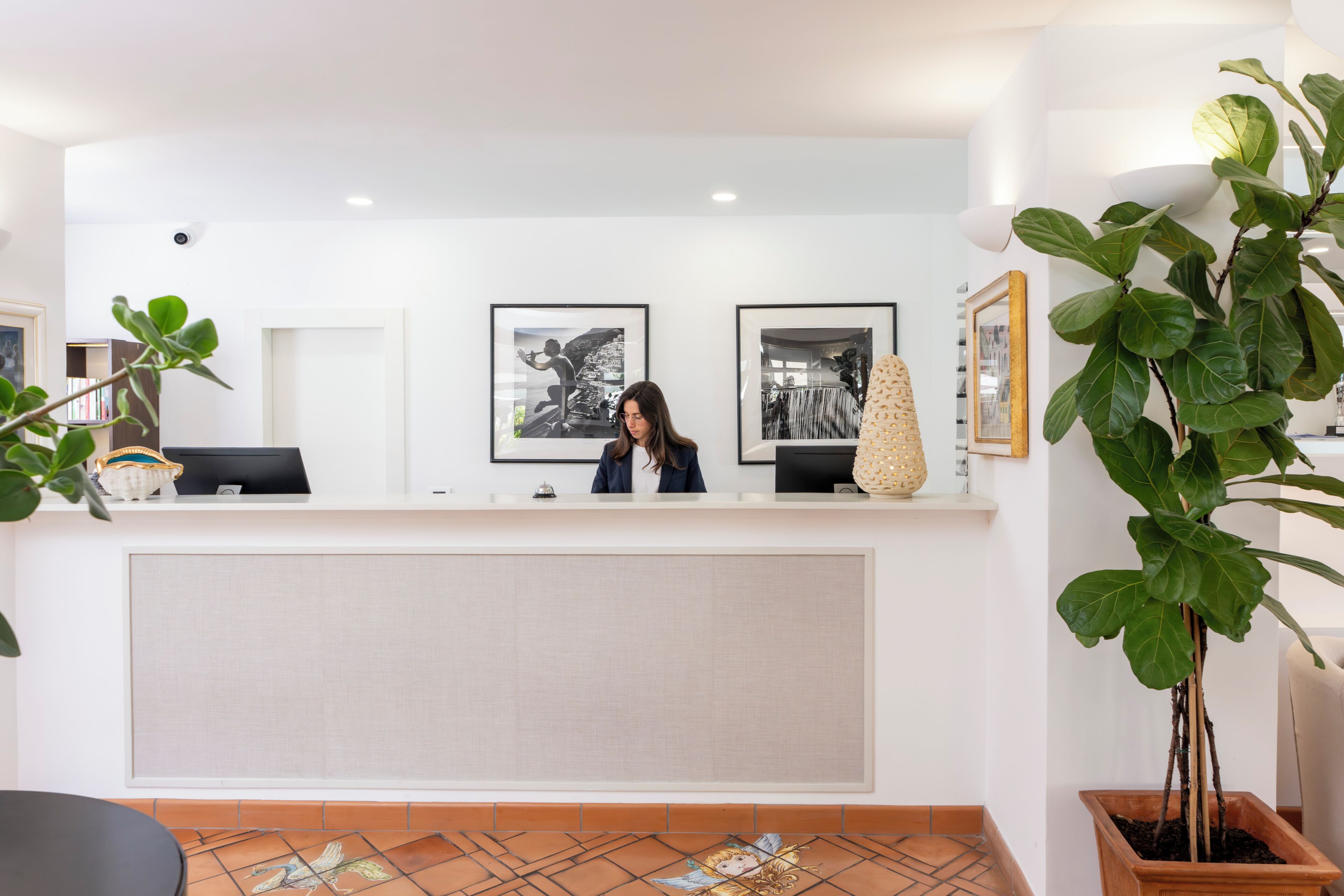 Una recepción con recepcionista, cuadros enmarcados en la pared y plantas en macetas.