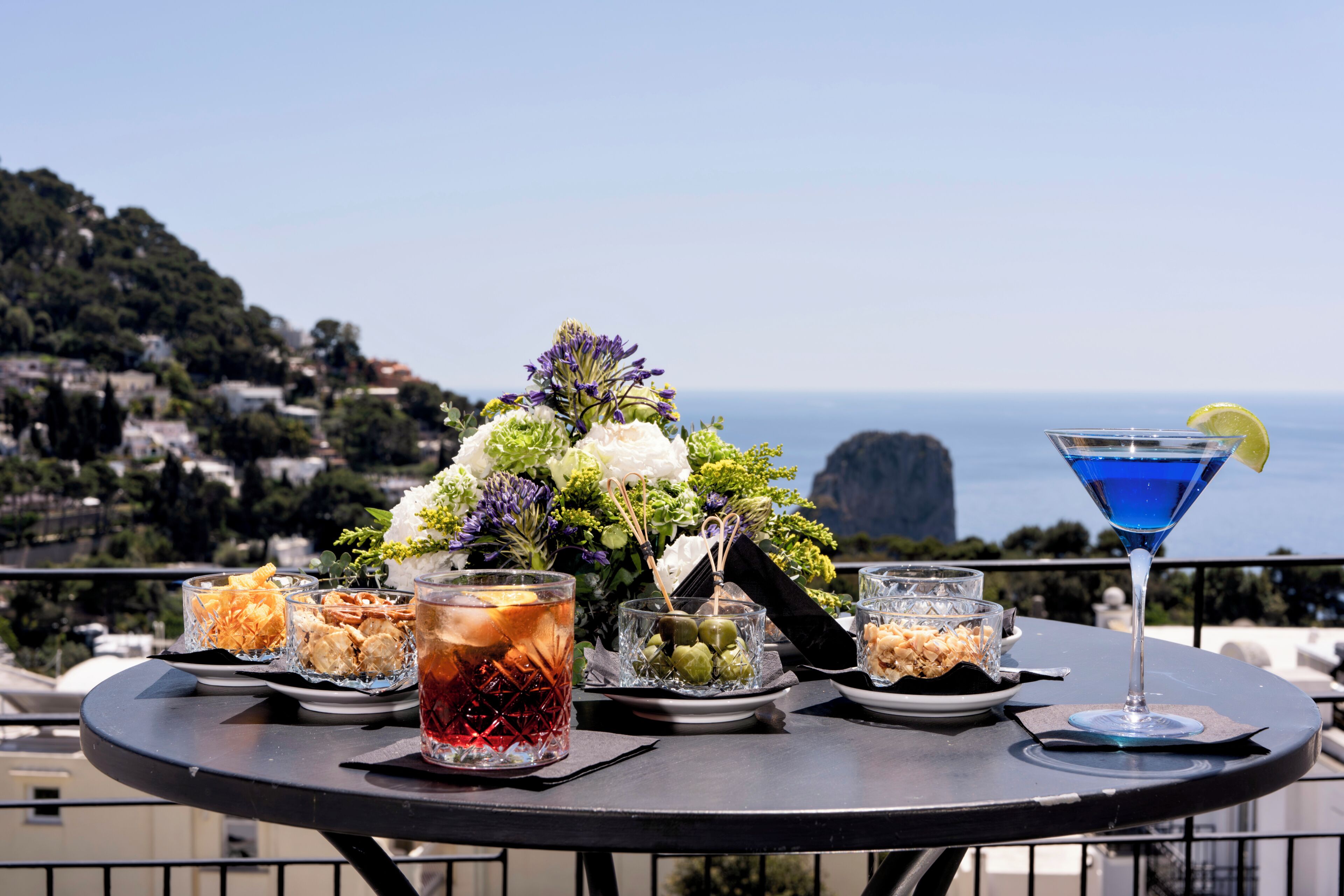 Una mesa servida con diversas bebidas y aperitivos, con vistas a un paisaje costero.