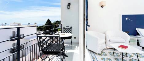 A balcony with a table and chairs, a sofa, and a view of the sea.