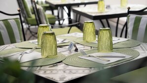 A dining area with tables set for two, each with a green placemat, a white napkin, cutlery, and a glass with a textured pattern. - Hotel Regina Cristina  (Capri)